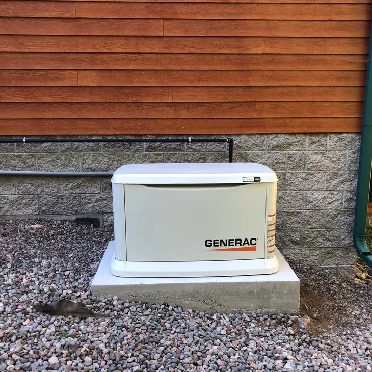 Generac air-cooled standby generator on a concrete pad beside a wood-sided home