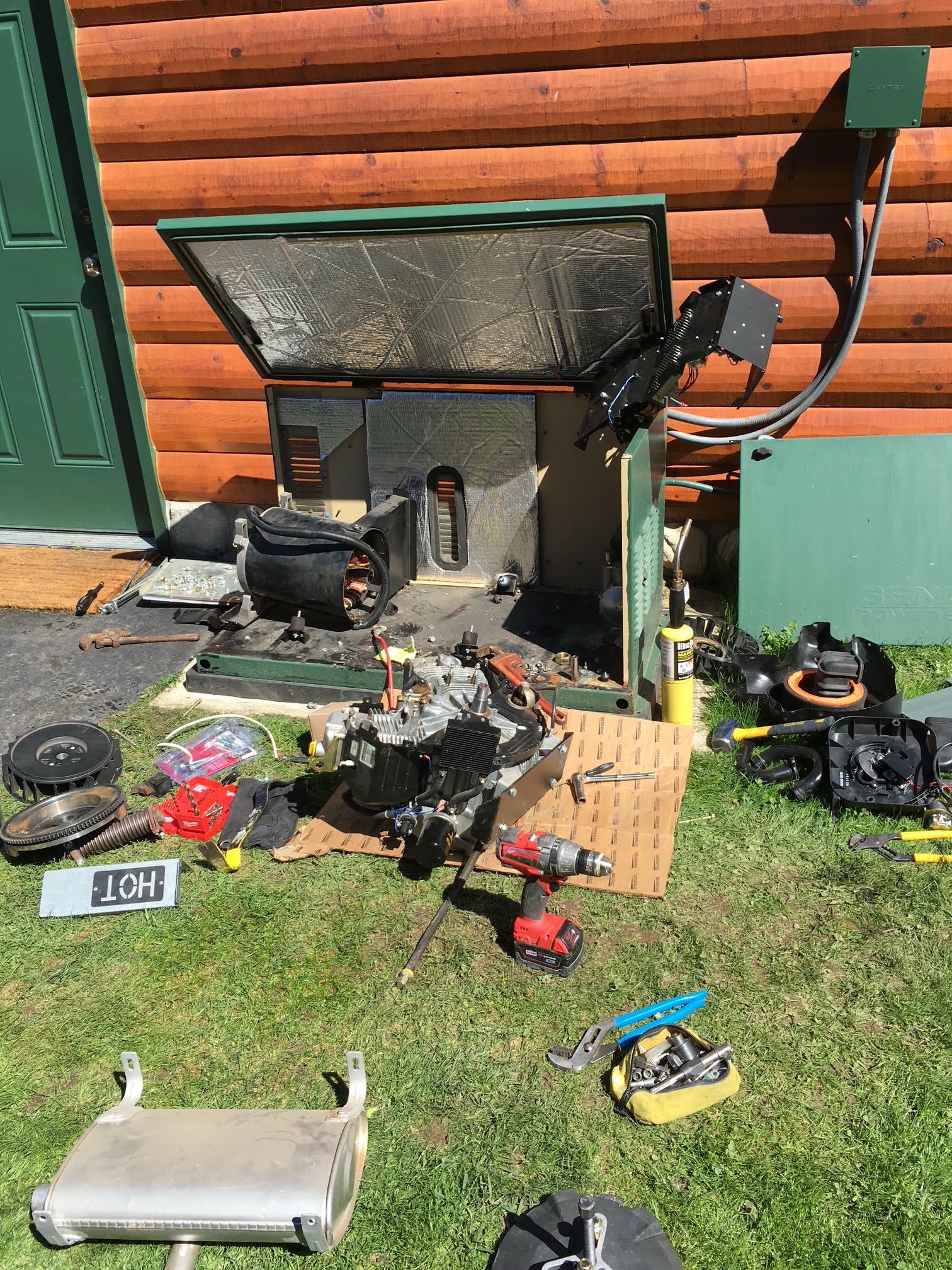 Generac generator opened for repair beside a log cabin with parts and tools laid out