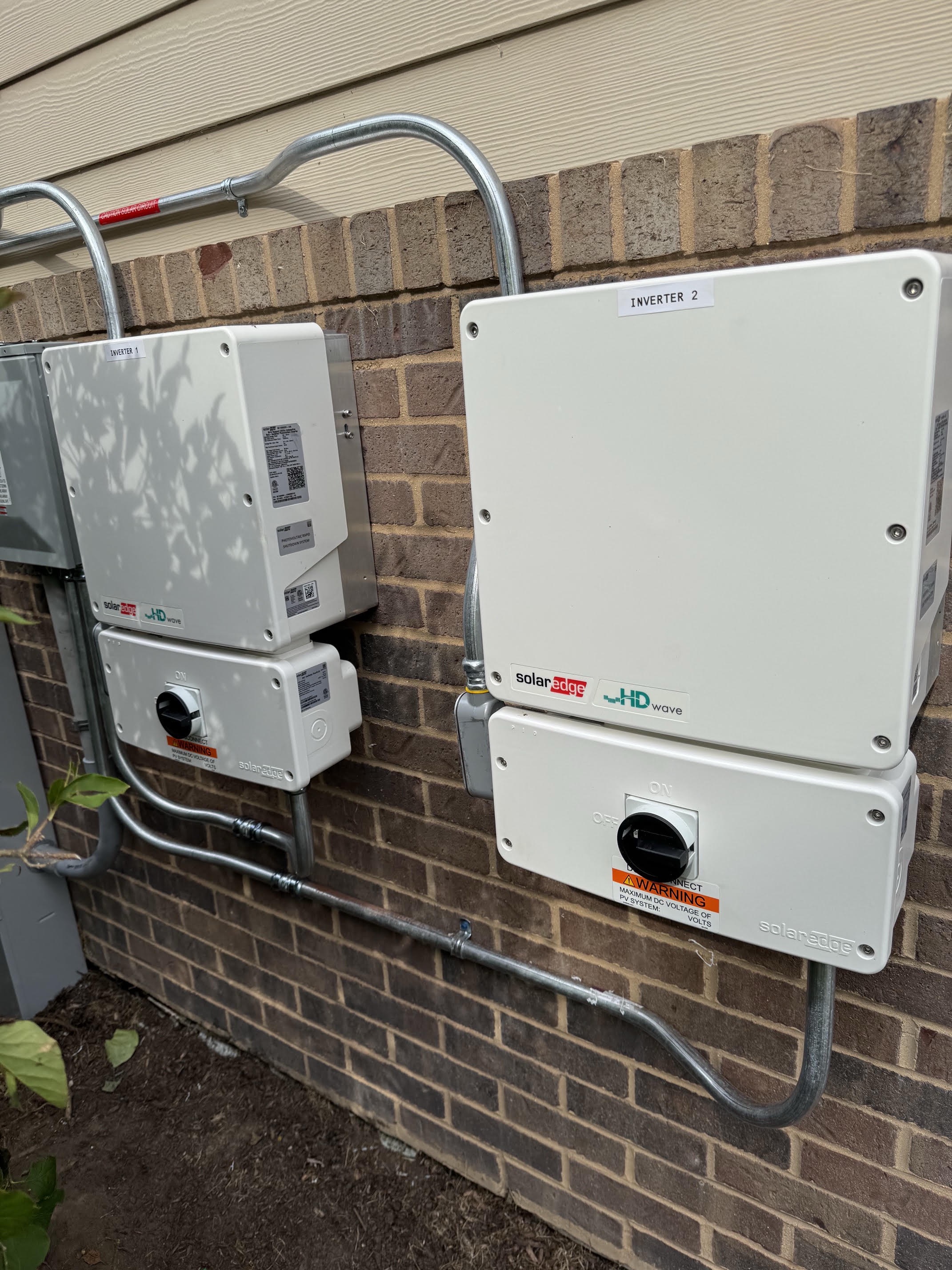 Two SolarEdge HD-Wave inverters and disconnects mounted and wired on a brick wall